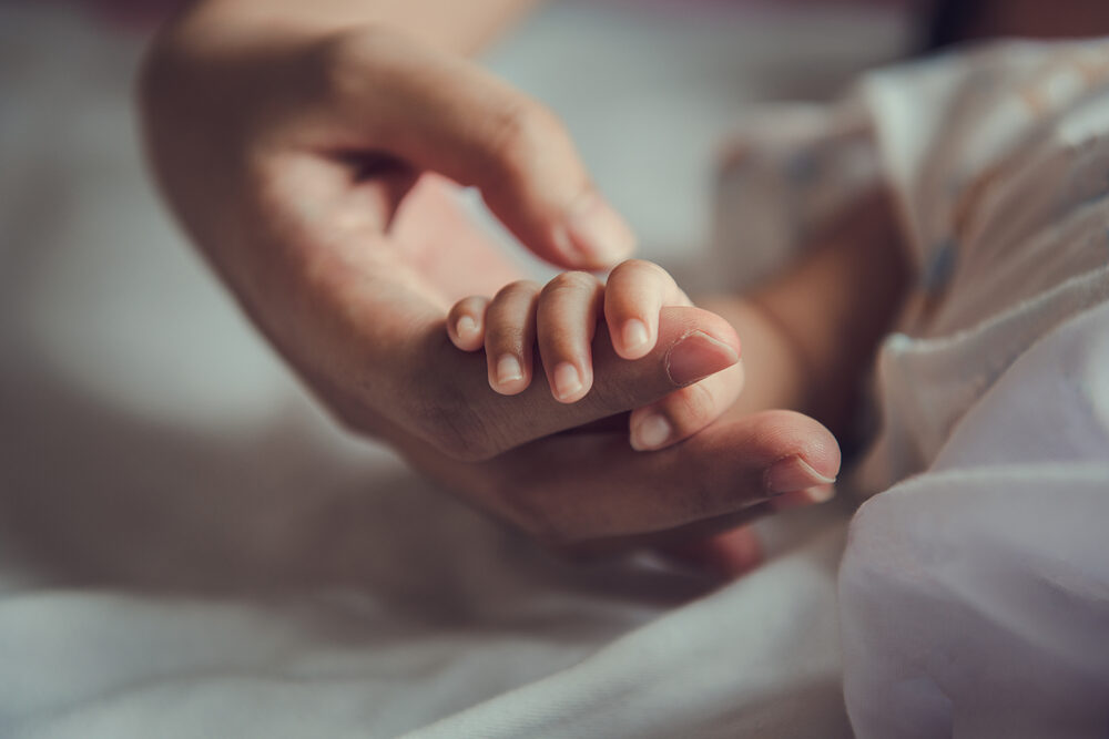 A newborn baby's hand wrapped around its mother's finger